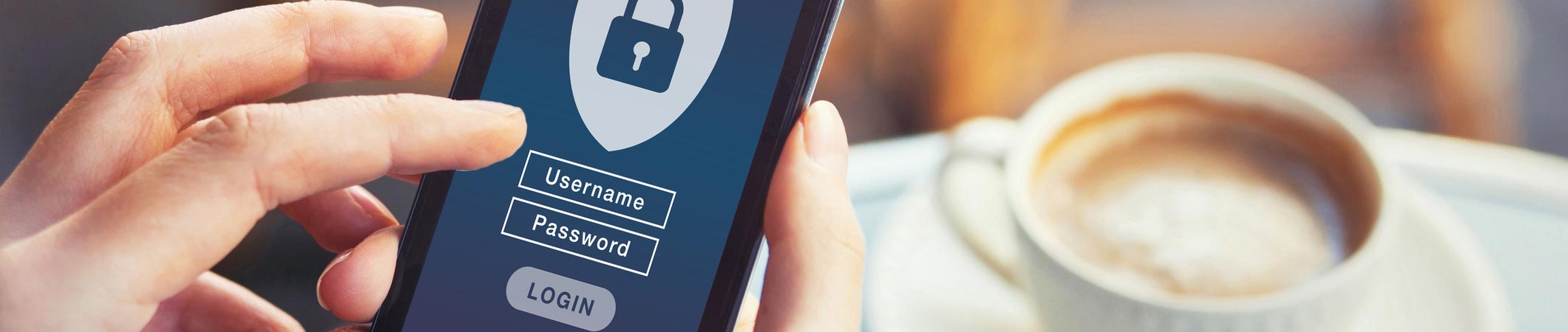 Hand mit Smartphone, Login-Maske mit Benutzername und Passwort neben Kaffeetasse – Symbol für sicheren Online-Zugang.