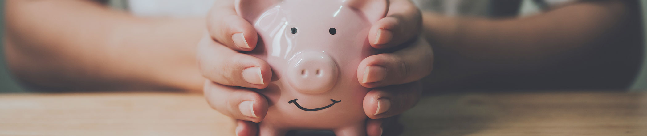 Hände umklammern rosa Sparschwein mit lächelndem Gesicht – Symbol für Ersparnisse und finanzielle Sicherheit.